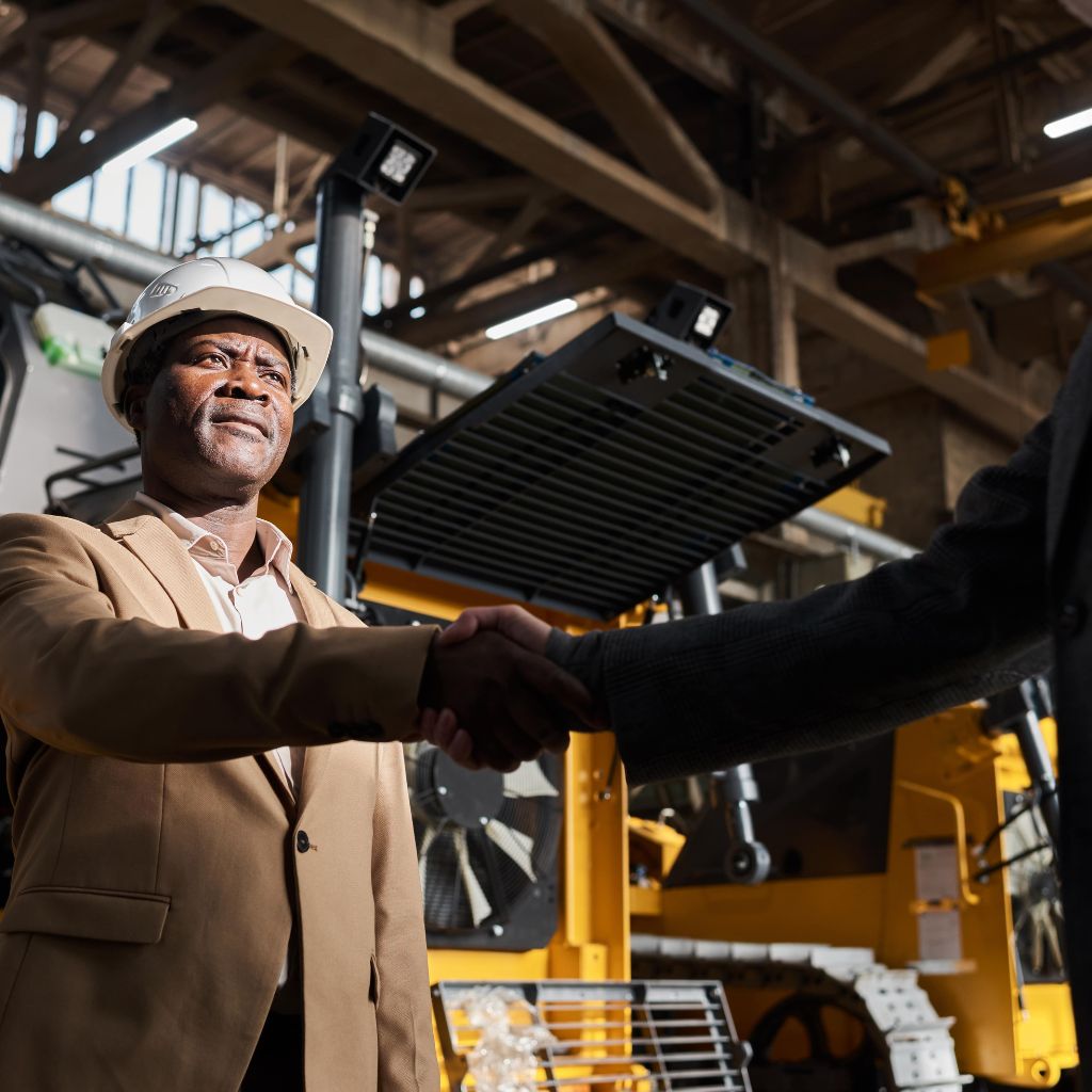 A man in a tan suit shakes hands with someone out of frame.